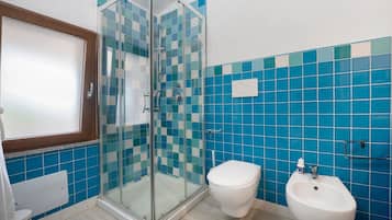 A bathroom with a glass shower enclosure, a toilet, and a bidet.