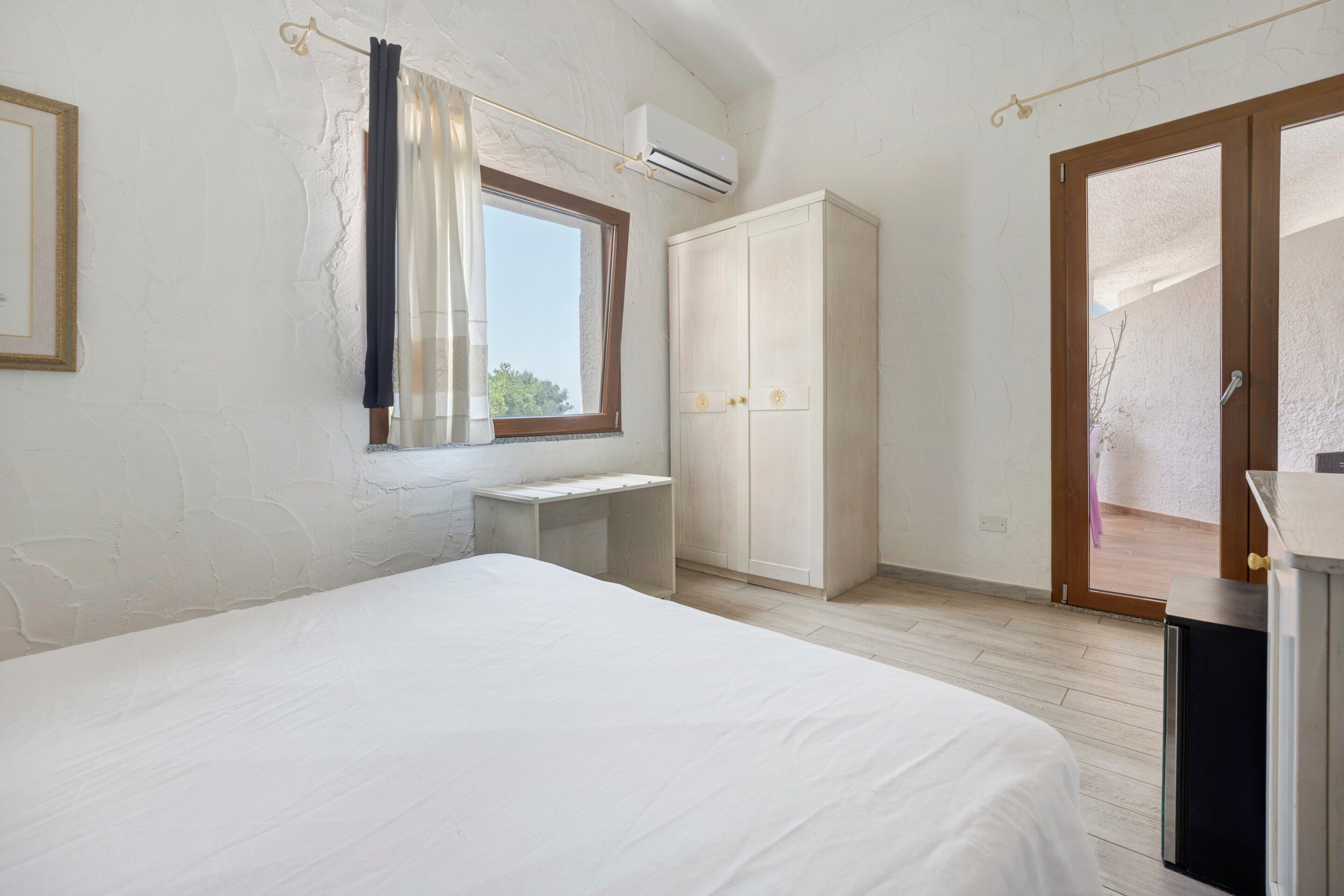 A bedroom with a bed, a desk, a wardrobe, and an air conditioning unit.