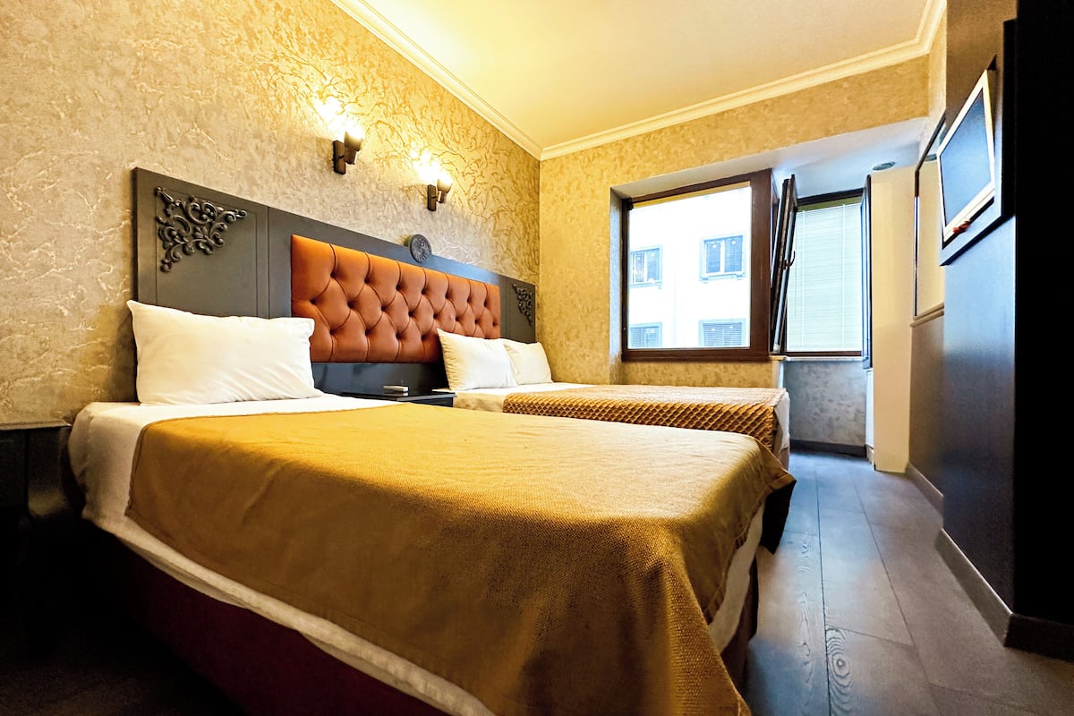 A hotel room with two beds, a large window, and a door leading outside.
