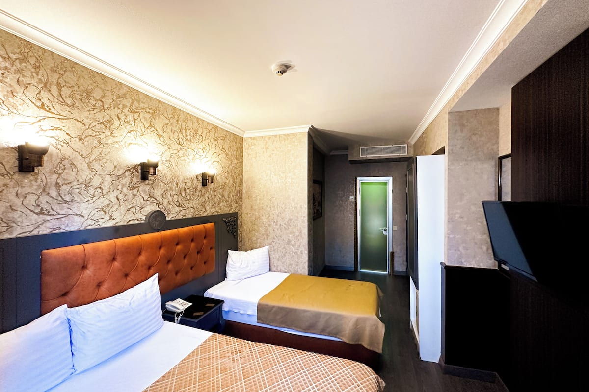 A hotel room with two beds, a television, a minibar, and a bathroom visible through a door.