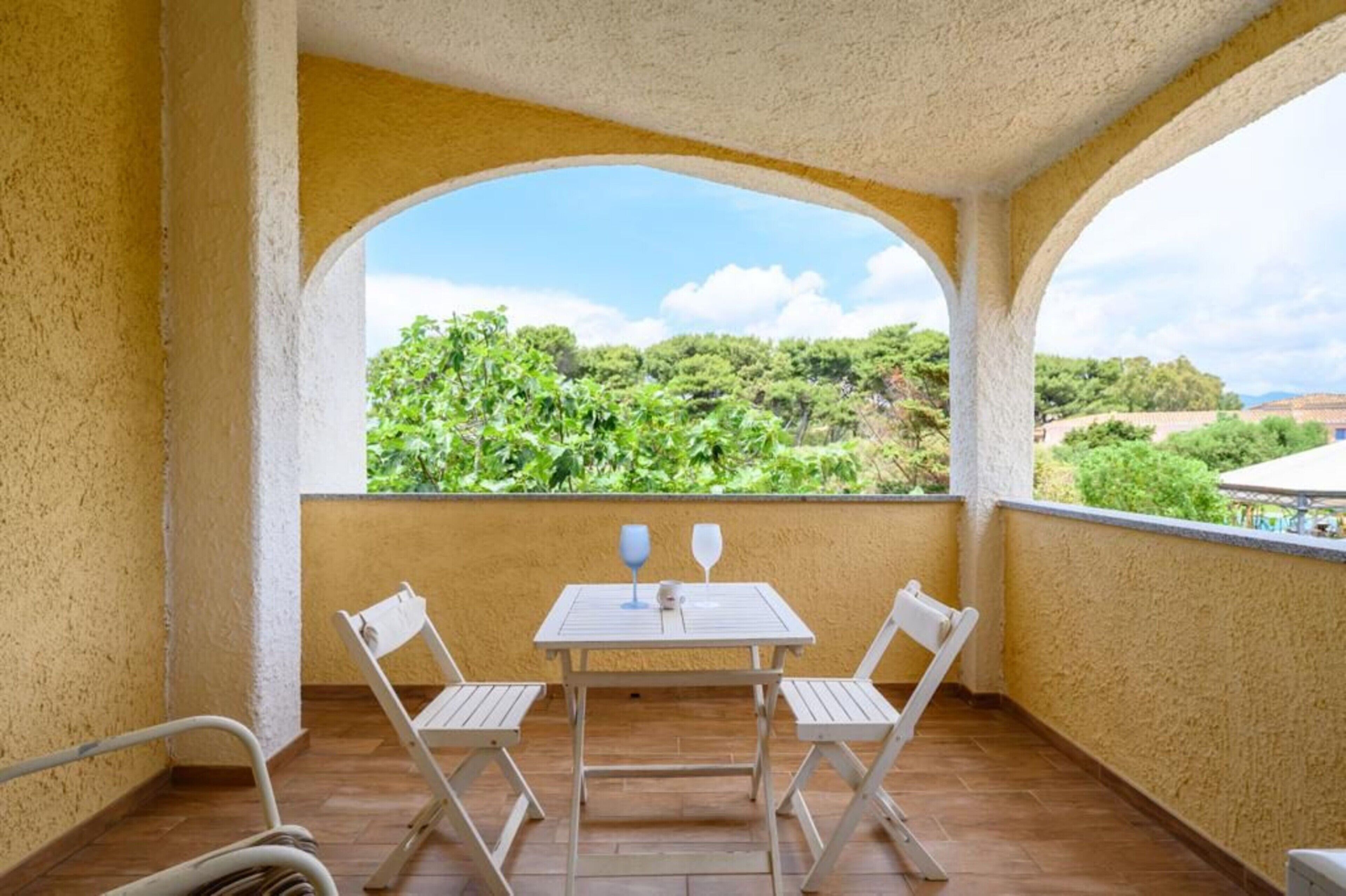 A balcony with a table and two chairs, overlooking a lush green landscape.
