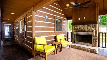 A log cabin interior with a stone fireplace, wooden furniture, and a ceiling fan.