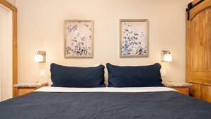 Quarto com cama, duas mesas de cabeceira, duas luminárias fixadas na parede e duas obras de arte com flores emolduradas.