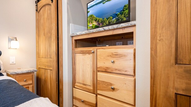 Quarto com cama, guarda-roupa de madeira e televisão sobre uma estante de mármore.