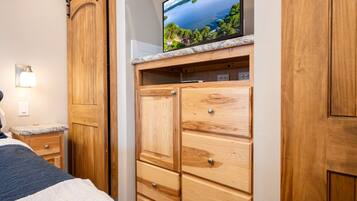 A bedroom with a bed, wooden wardrobe, and a television on a marble shelf.