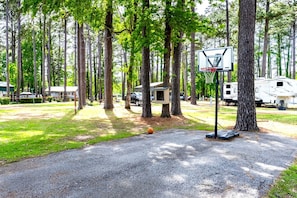 Basketbalveld met een ring, omringd door bomen en campers.