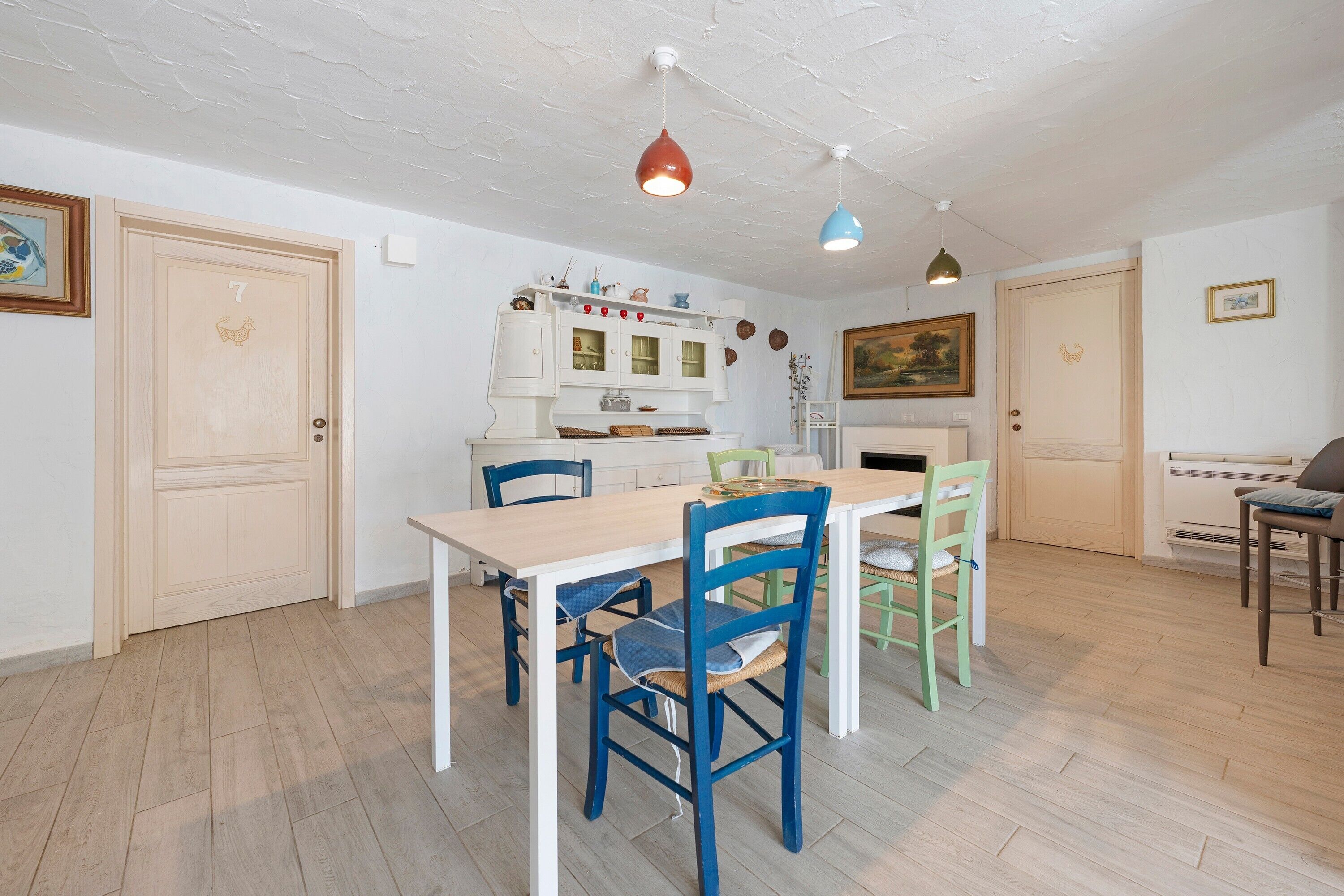 Una zona pranzo con un tavolo e sedie in legno, un armadietto bianco con ante in vetro e un quadro appeso al muro.