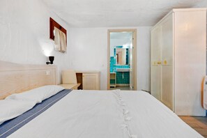 A bedroom with a bed, a bedside table, a chair, a wardrobe, and a bathroom visible through an open door.