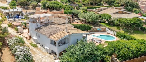 A villa with a swimming pool, surrounded by lush greenery and a hilly landscape.