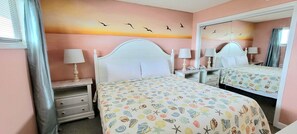 A bedroom with two beds, a nightstand with a lamp, a dresser, and a mirror. - Oceanfront bliss awaits in this 1-bedroom condo 0804 (Carolina Beach)