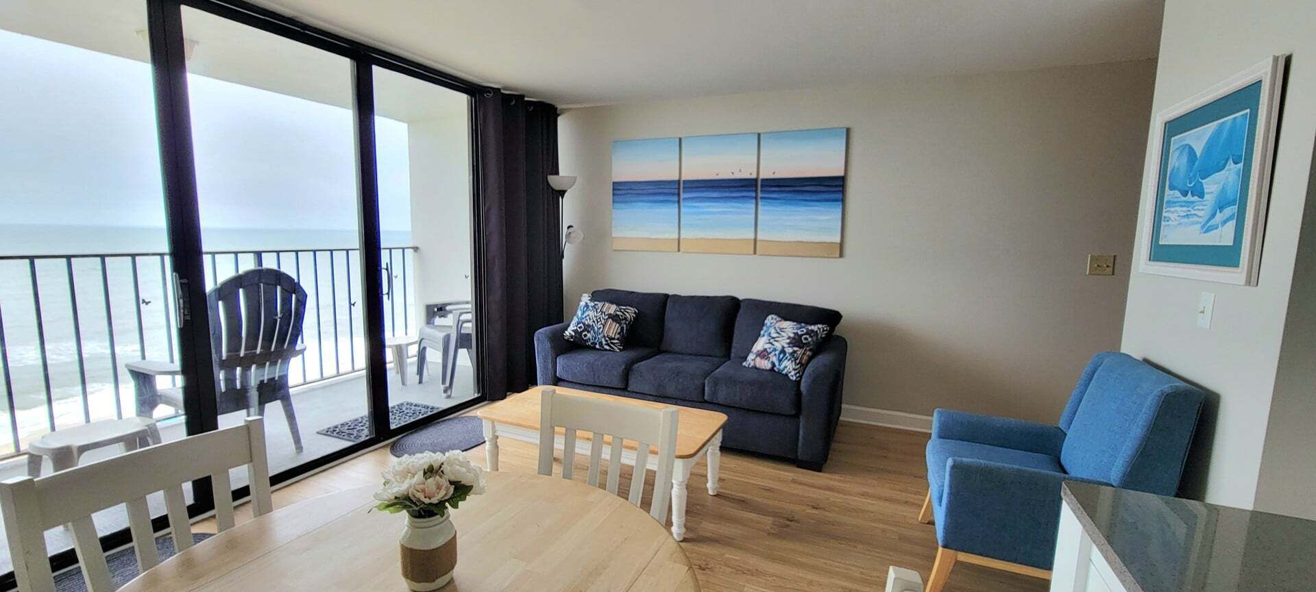 Ein Wohnzimmer mit Sofa, Couchtisch, Esstisch mit Stühlen, Balkon mit Geländer und einem Bild an der Wand.