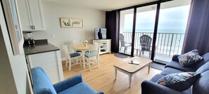 Une pièce avec un balcon, un coin repas, un canapé et un espace cuisine.