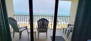 A balcony with chairs and a table, overlooking a beach with the ocean and a cloudy sky. - Oceanfront bliss awaits in this 1-bedroom condo 0804 (Carolina Beach)
