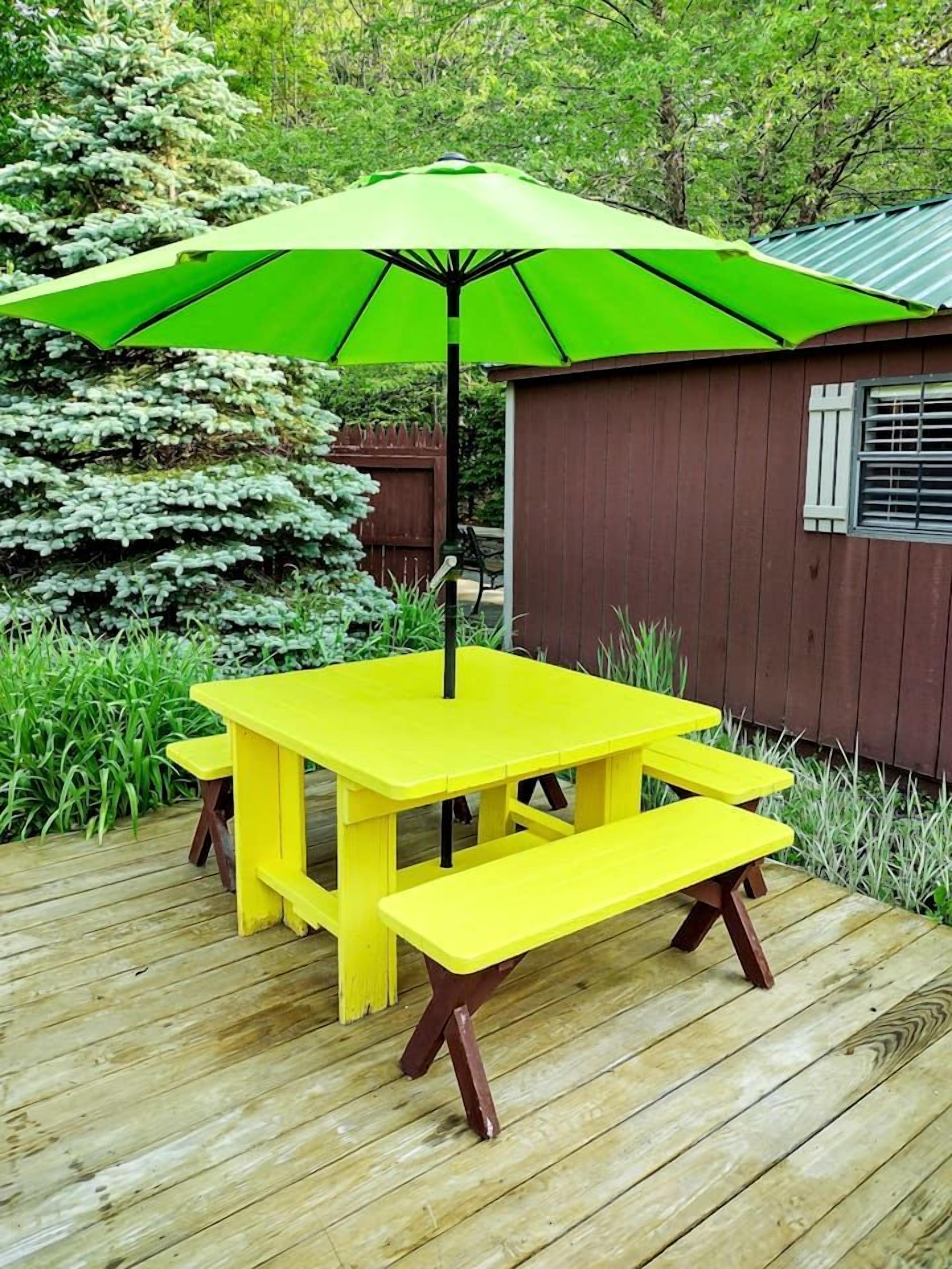 A yellow picnic table with benches and a green umbrella on a wooden deck.