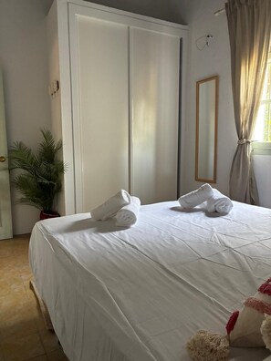 Ein ordentlich bezogenes Bett mit Handtüchern, einem Blumentopf, einem Kleiderschrank und einem Spiegel.