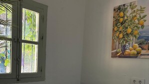 A room with a white table, a green pillow, a window with curtains, and a painting of fruit on the wall. - Exclusive three-bedroom home just a few minutes from the beach. (El Puerto de Santa María)