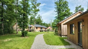 Une rangée de cabanes en bois, avec des allées de gravier, entourées d’arbres.