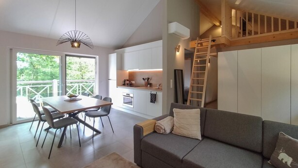 Un intérieur moderne comprenant un espace repas, une cuisine et une chambre à l’étage, accessible par un escalier en bois.