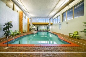 An indoor swimming pool with a brick floor, surrounded by green chairs, and a view of the sky through the ceiling. - Shores of Panama 231 - Beautiful 3 Bedroom (Sleeps 8).  Same Floor Parking! No Elevators Needed (Panama City Beach)