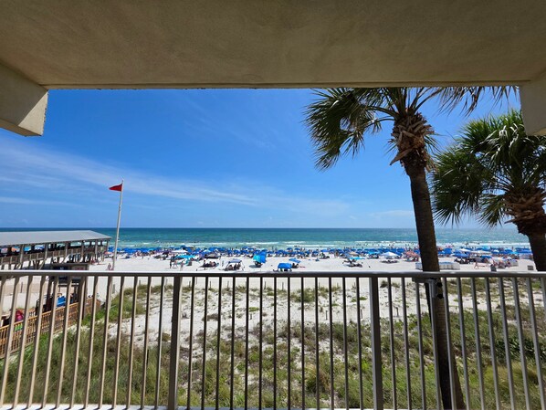 Blick auf einen Strand vom Balkon mit Geländer, Palmen und blauem Himmel.