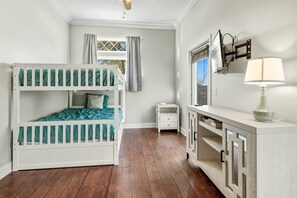 A room with a bunk bed, a small bedside table, a desk with a lamp, and a window with curtains. - Coastal Beach Home with BBQ Grill & Kids Playground in Panama City Beach, Florida (Panama City Beach)