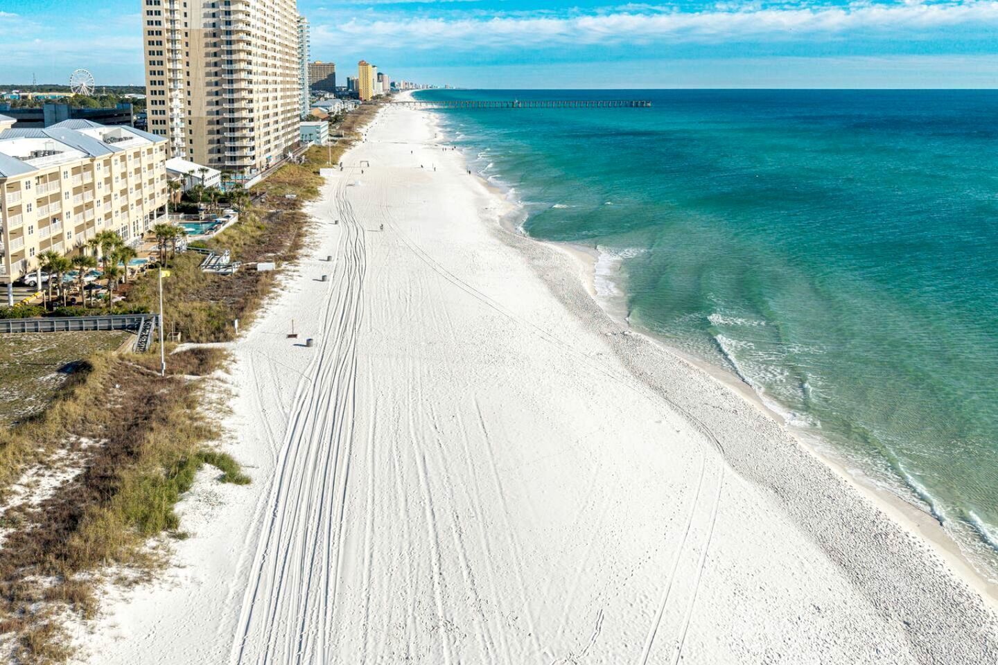 A beach with a long stretch of sand, a pier extending into the ocean, and a high-rise hotel on the left.