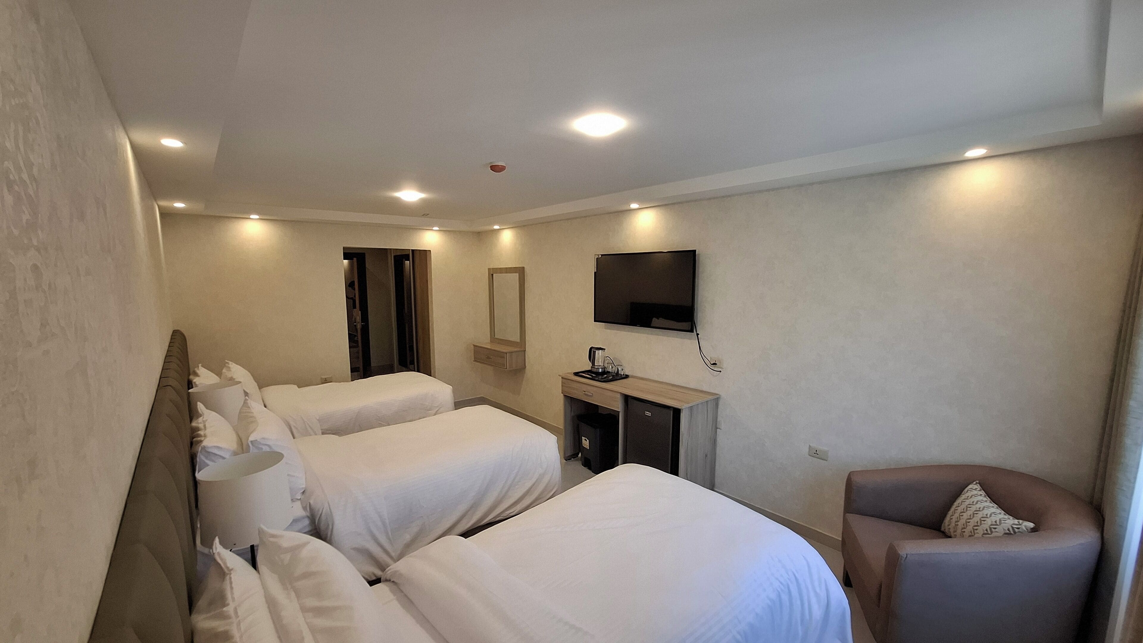 Een hotelkamer met twee bedden, een bureau met een televisie, een stoel en een kleine prullenbak.