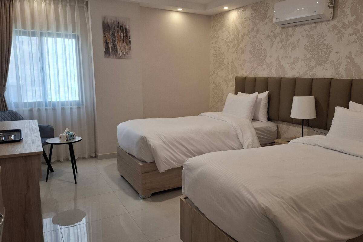 Een hotelkamer met twee bedden, een bureau, een stoel, een kleine tafel en een airconditioning.