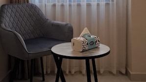 Una habitación con un sofá gris, una mesa redonda y una ventana con cortinas de gasa.