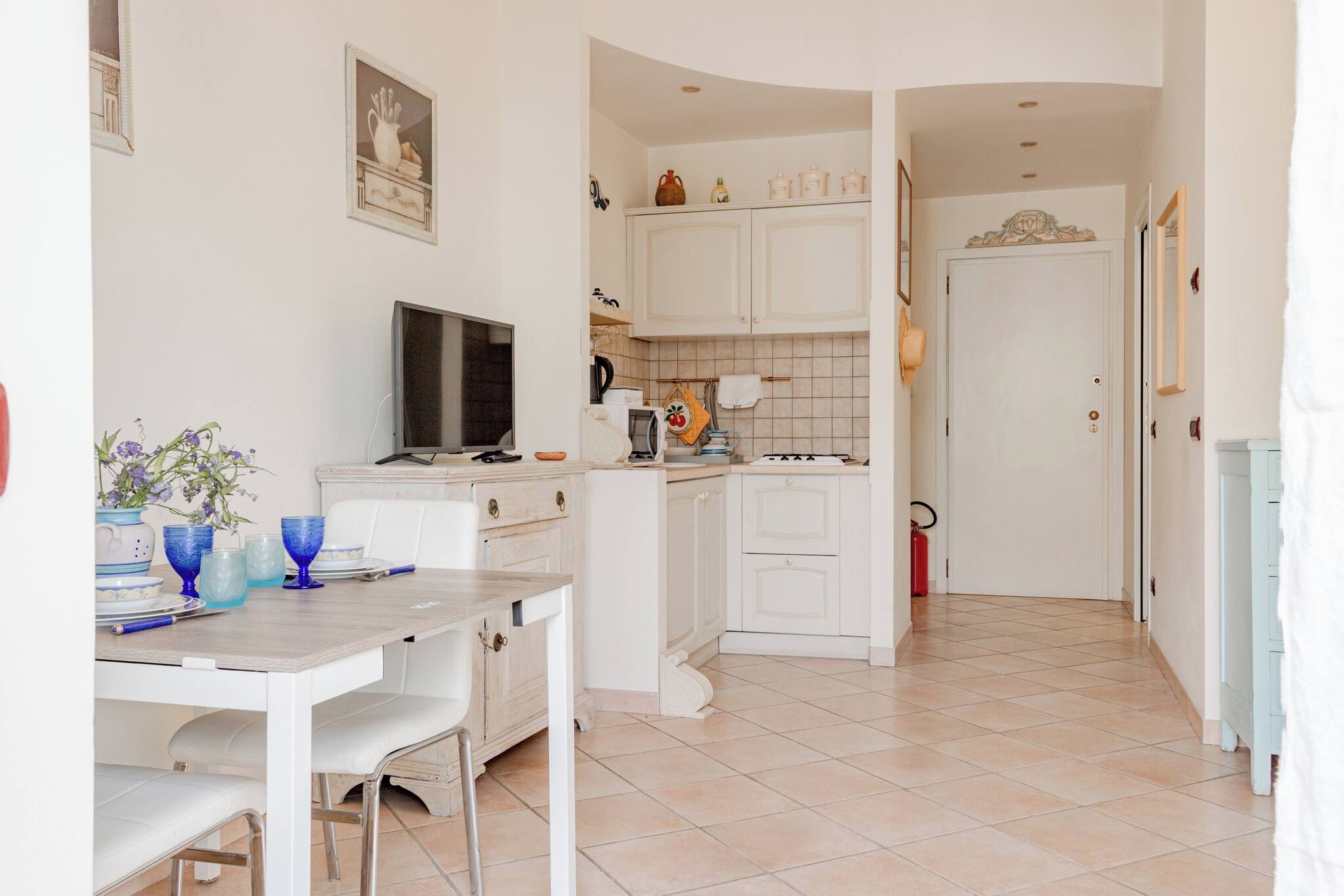 Una cocina compacta con armarios blancos, una mesa de comedor con sillas y un televisor.