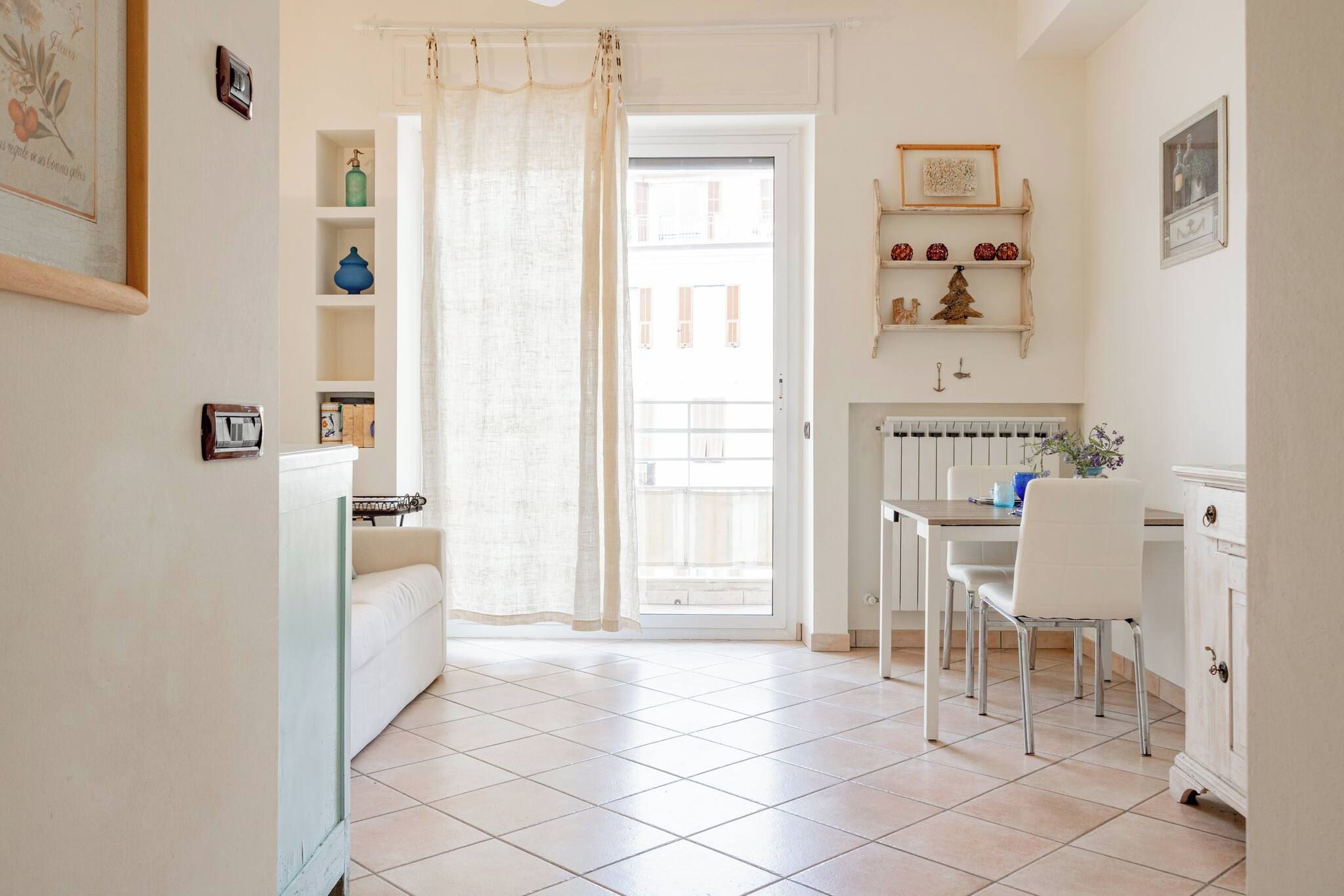 A bright kitchen with a dining area, white tiled flooring, and a view through a door.