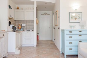 A kitchen with white cabinets, a microwave, and a gas stove. There is a hallway leading to a door. - CASA GIULIA - Centro - Sanremo (Sanremo)