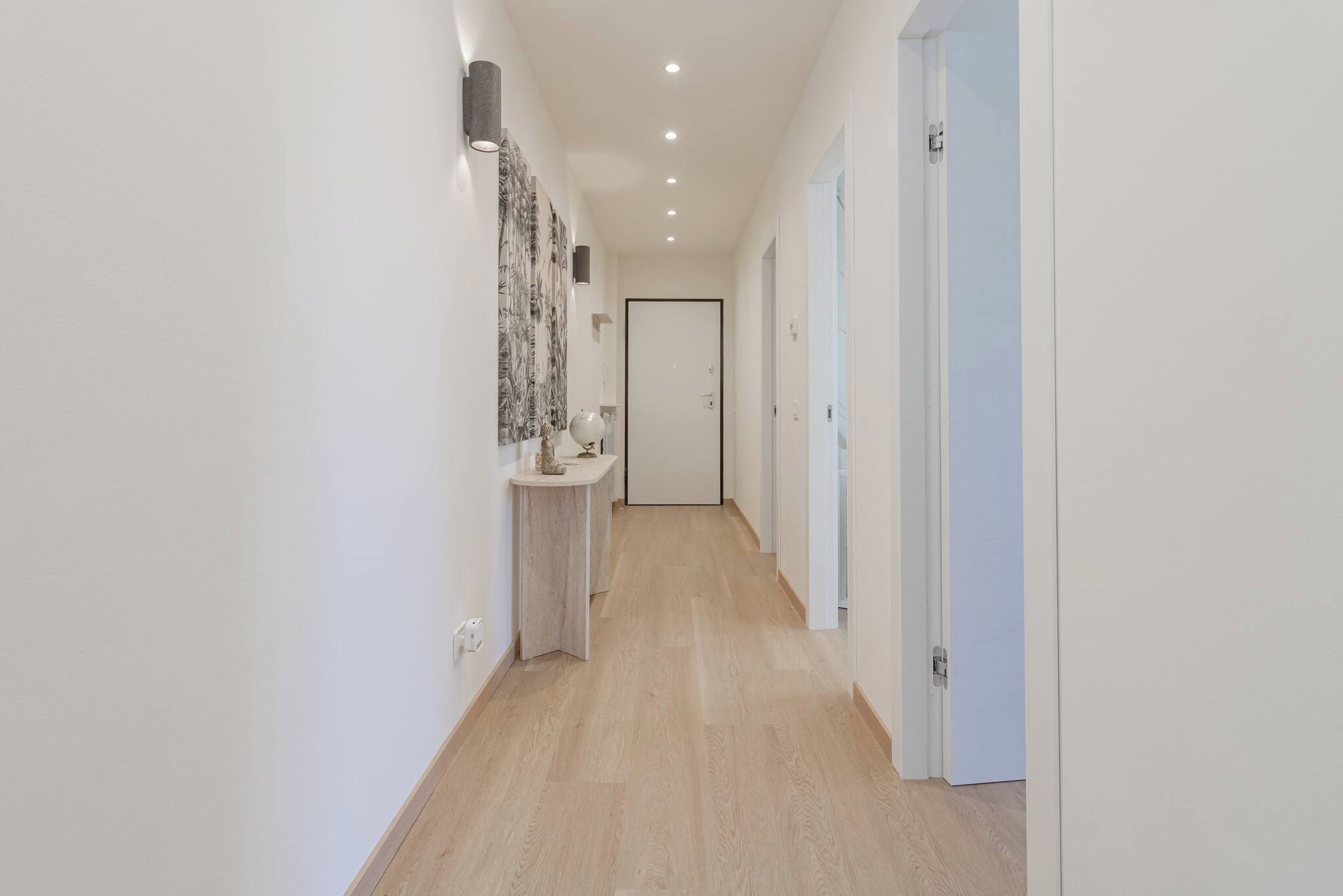 Un couloir avec un plancher en bois, des murs blancs et une porte au fond.