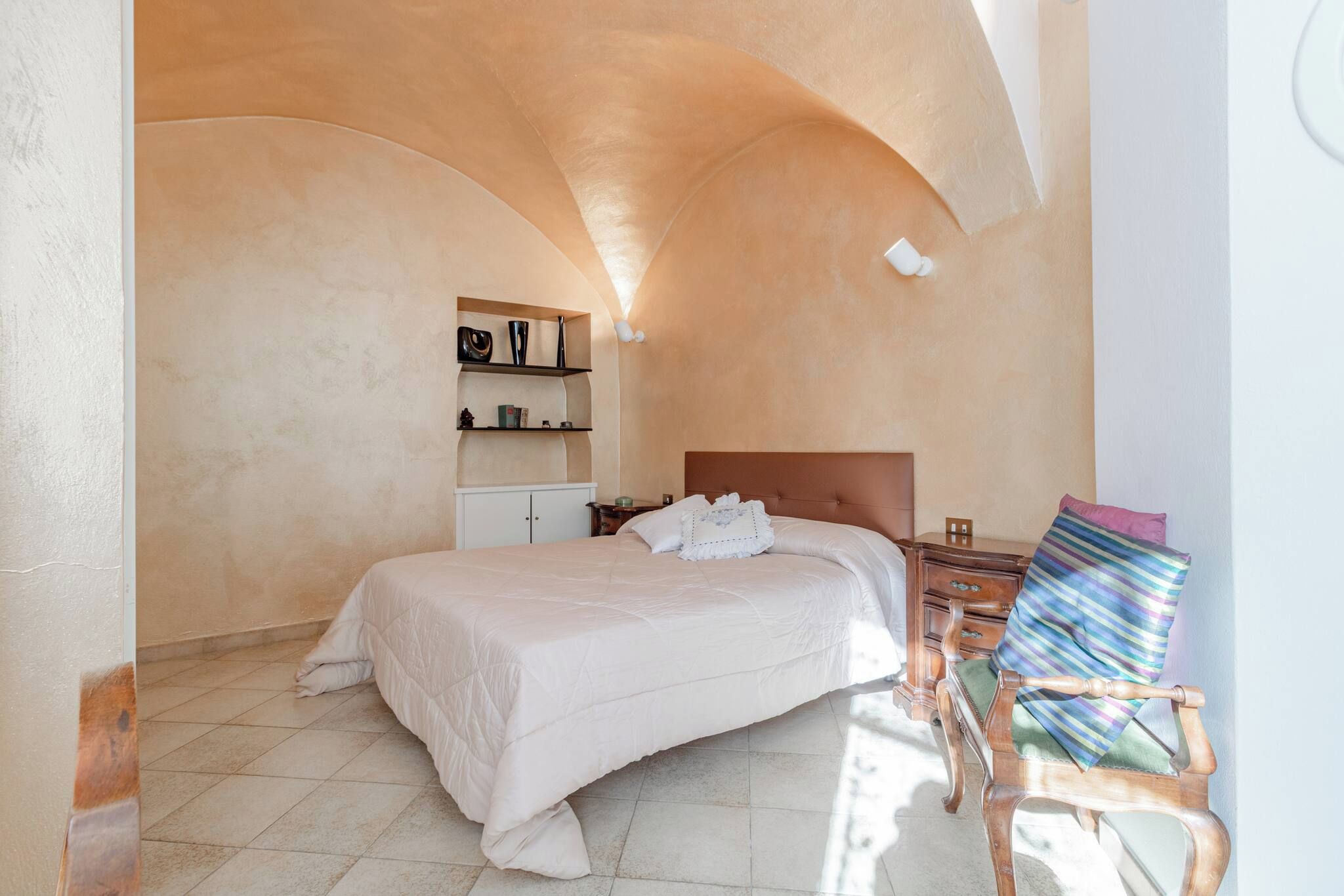 Une chambre à coucher comprenant un lit, une table de chevet, une chaise et une étagère avec des objets décoratifs.