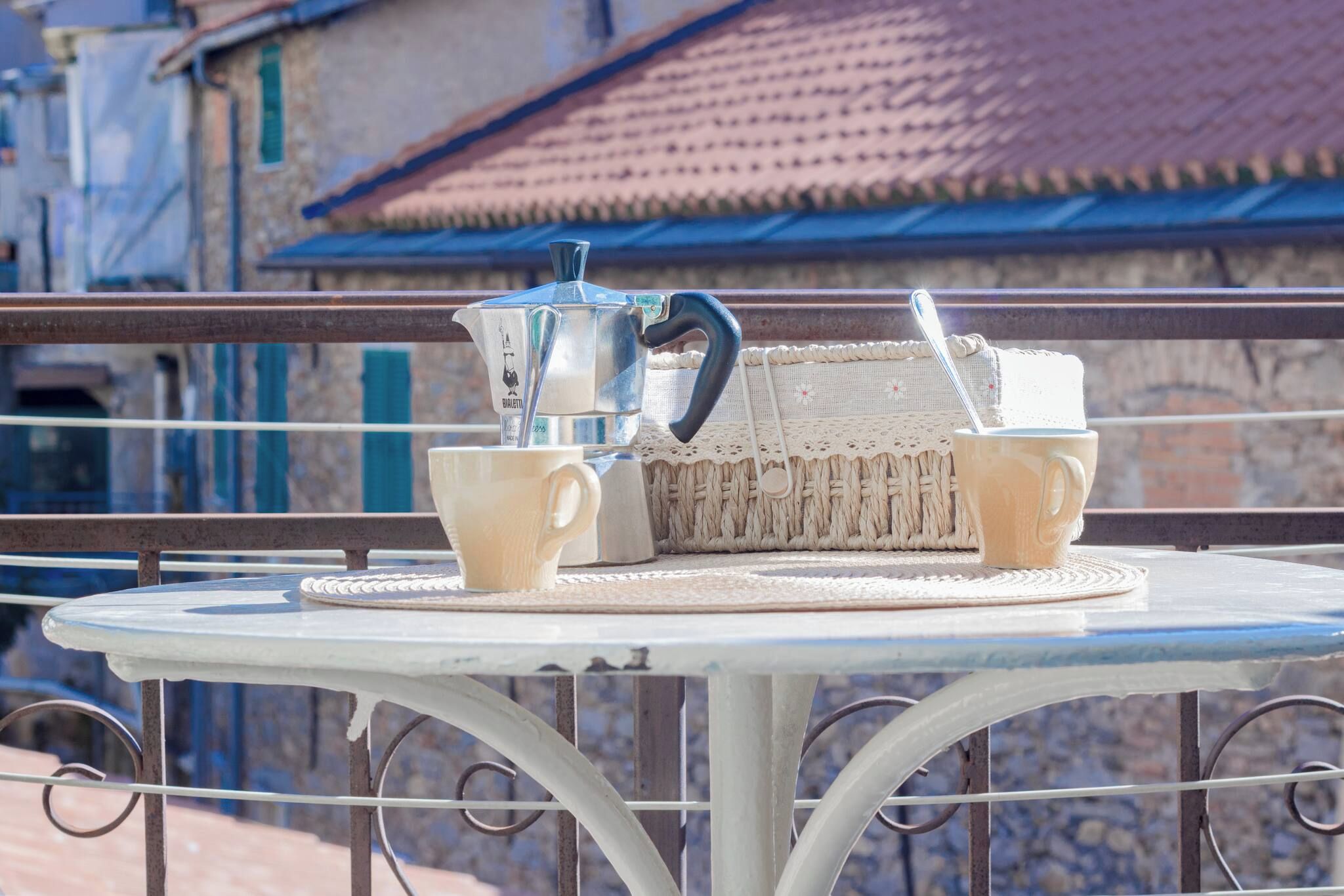 A round metal table with a woven basket and two cups, a metal pitcher, and a spoon on it.