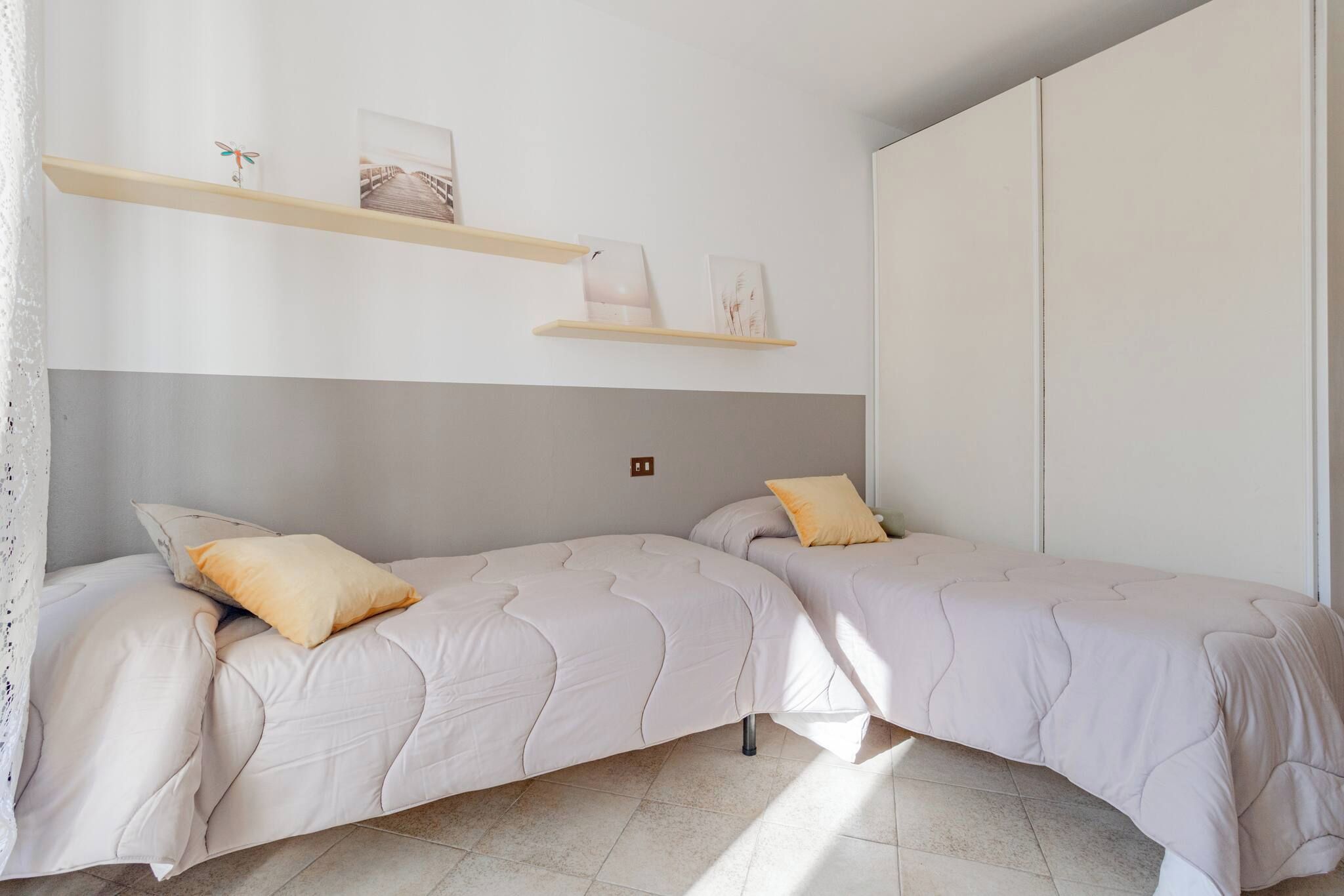 A bedroom with two beds, a wooden shelf with pictures, and a large wardrobe.