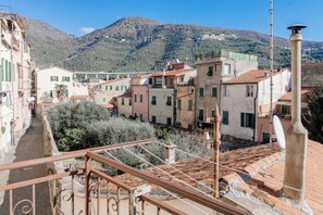 A narrow street with traditional buildings, a metal railing, and a mountainous backdrop. - CA' IN TE L'AIA - Taggia Centro (Taggia)
