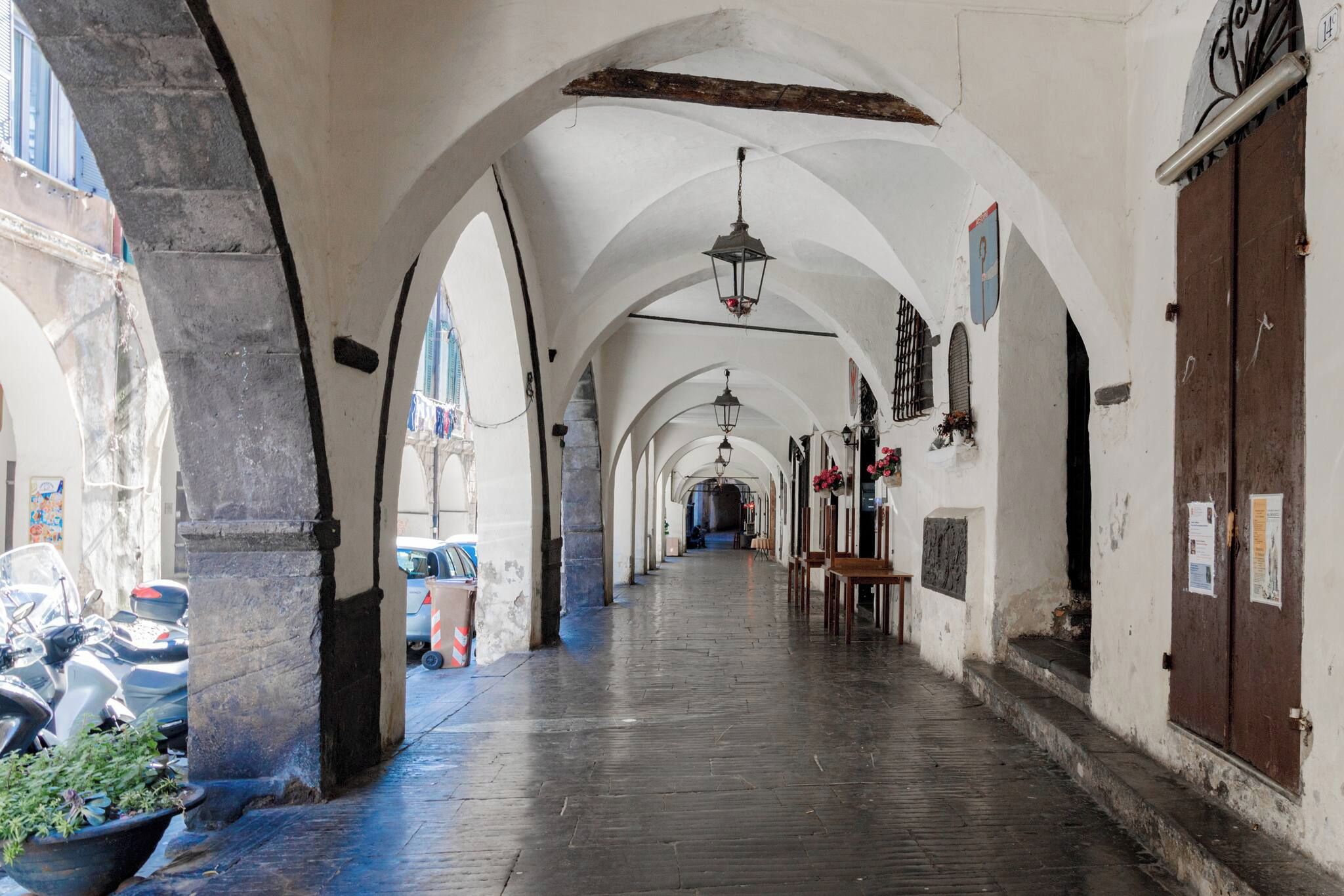 A corridor with arches, a hanging light fixture, and a wooden door.