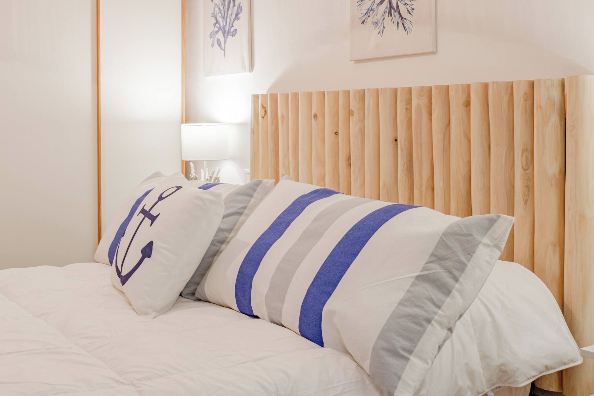Una cama con ropa de cama blanca y almohadas a rayas, un cabecero de madera y una mesita de noche con una lámpara.