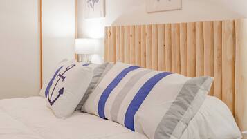 Una cama con ropa de cama blanca y almohadas a rayas, un cabecero de madera y una mesita de noche con una lámpara.