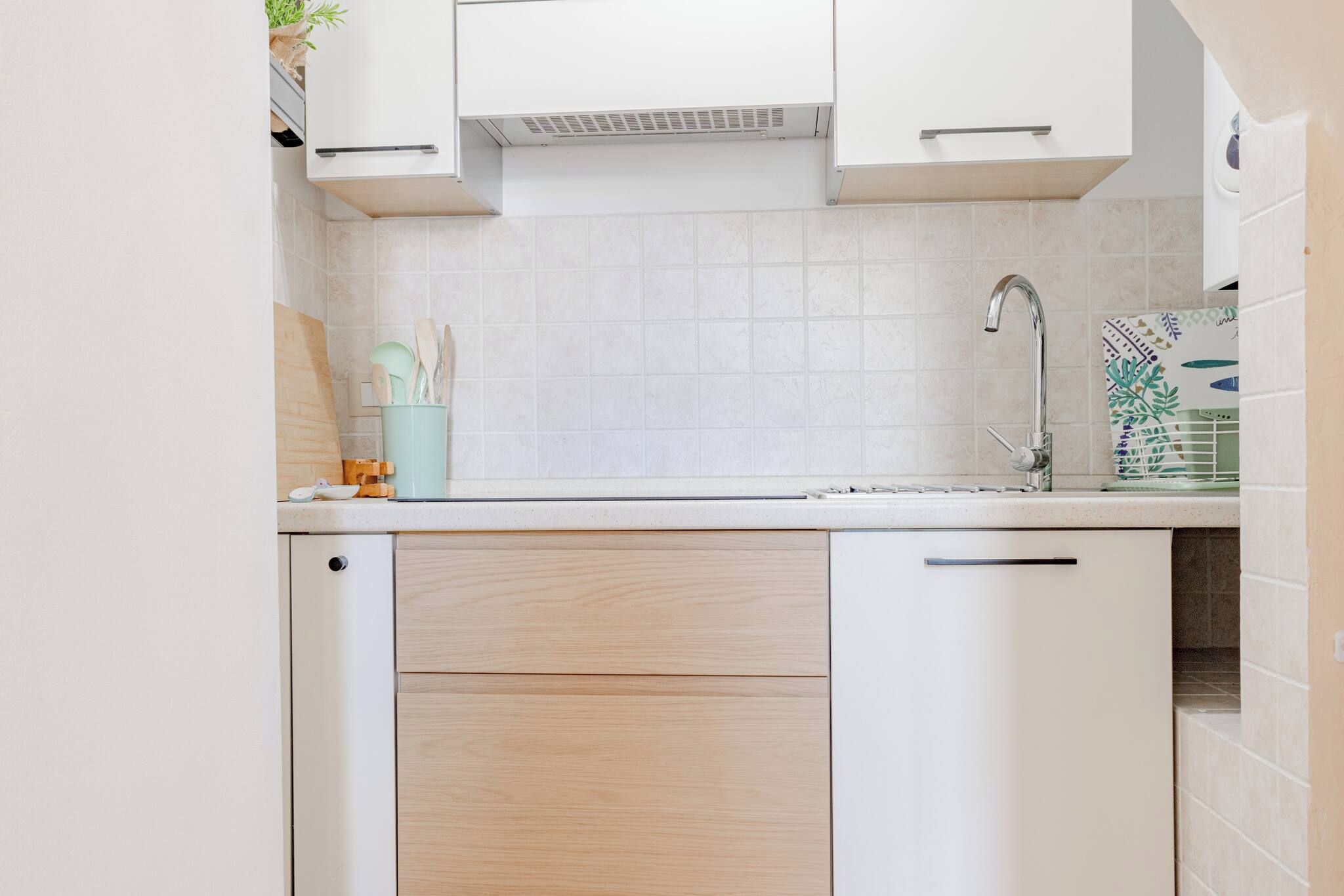 Una cocina con gabinetes blancos, un lavamanos de acero inoxidable y un salpicadero de azulejos.