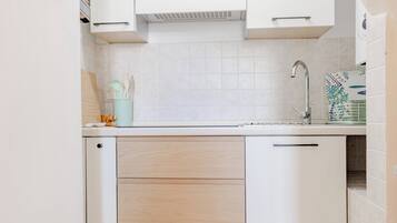Una cocina con gabinetes blancos, un lavamanos de acero inoxidable y un salpicadero de azulejos.