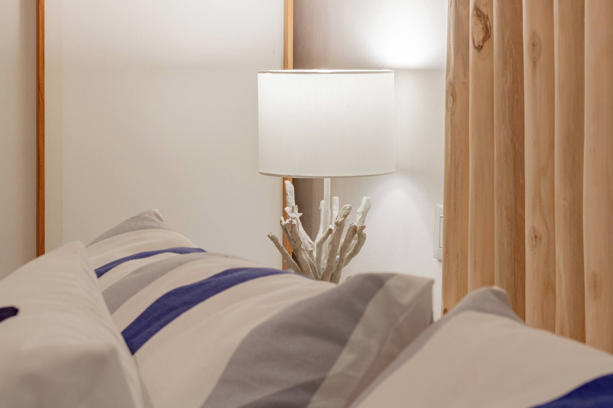 Habitación de hotel con cama, mesita de noche con lámpara y paneles de madera.