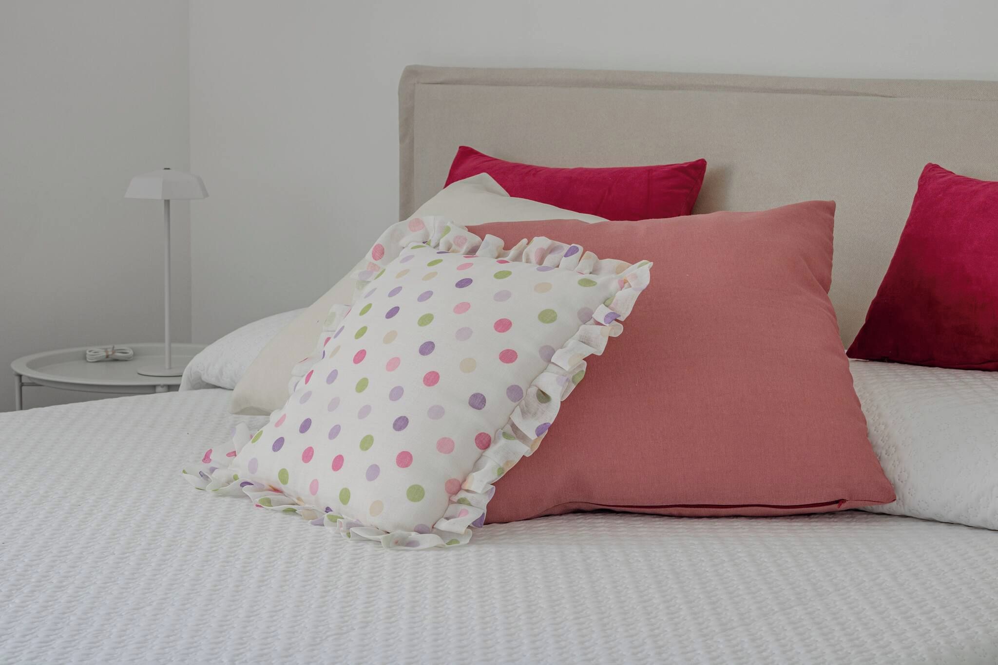 A bed with white bedding and multiple pillows, including a polka-dotted one and two solid-colored ones.