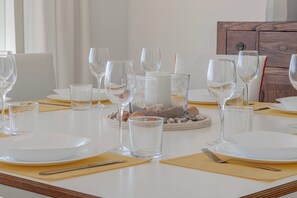 Une table à manger dressée avec de l’assiette blanche, des verres transparents et un centre de table composé de coquillages et d’une bougie.