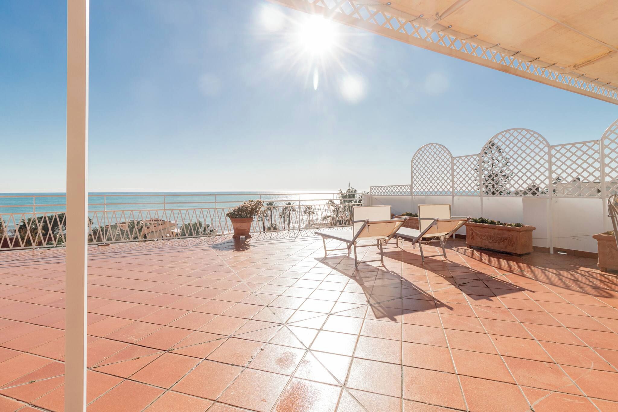 A terrace with a view of the sea, featuring tiled flooring, outdoor furniture, and a white lattice fence.