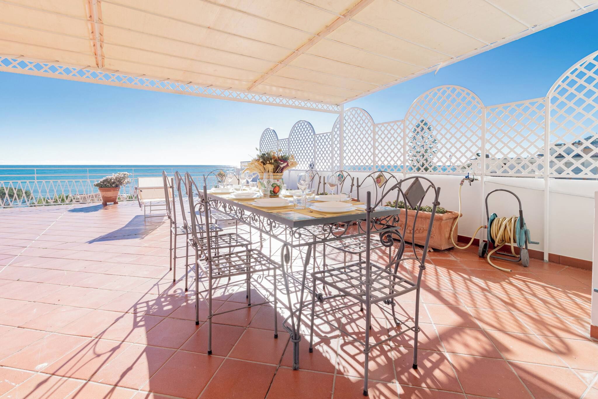 An outdoor dining area with a view of the sea, a table set for four, and a white lattice partition.