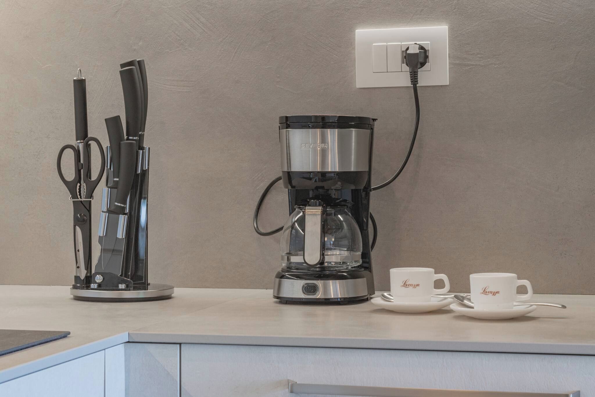 A kitchen counter with a coffee maker, a pair of scissors, and two cups.