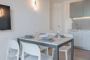 Ein moderner Essbereich mit einem für vier Personen gedecktem Tisch, weißen Stühlen und einer Küche im Hintergrund.