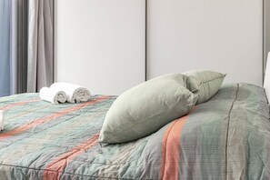 Un letto rifatto con copripiumino trapuntato e due cuscini, un asciugamano bianco arrotolato e una finestra con tende.